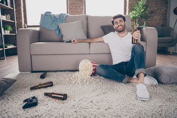 Photo of mixed race guy sitting carpet near sofa holding beer bottle popcorn floor having fun crazy...