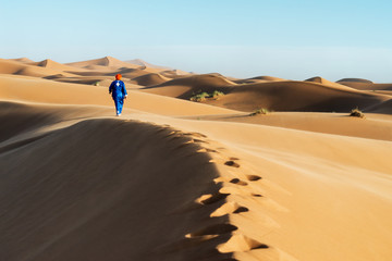 Fototapeta na wymiar Traditional dressed Moroccan man with turban walks on a sand dune in the Sahara desert.