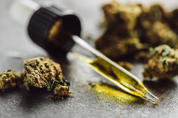 close up view of medical marijuana buds and dropper with hemp oil on stone surface