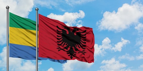 Gabon and Albania flag waving in the wind against white cloudy blue sky together. Diplomacy...