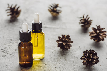 selective focus of bottles with natural oil near dry cones on grey stone surface