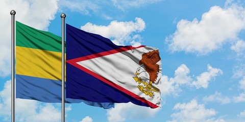 Gabon and American Samoa flag waving in the wind against white cloudy blue sky together. Diplomacy...