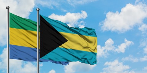 Gabon and Bahamas flag waving in the wind against white cloudy blue sky together. Diplomacy...
