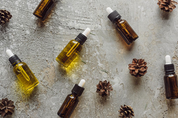 top view of bottles with natural oil near dry spruce cones on grey stone surface