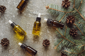 top view of bottles with natural oil near fir branches and dry cones on grey stone surface