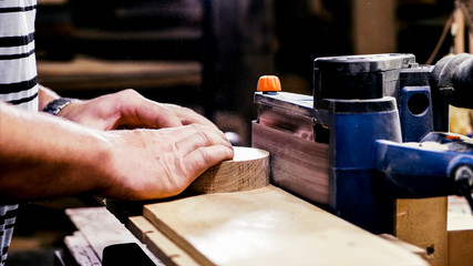 Closeup hands of male carpenter worker is grinds the wood detail. Craftsman polishing with grinding machine at wood workshop.