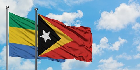 Gabon and East Timor flag waving in the wind against white cloudy blue sky together. Diplomacy concept, international relations.