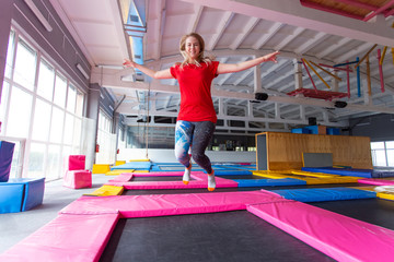 Fitness, fun, leisure and sport activity concept - Young happy woman jumping on a trampoline indoors