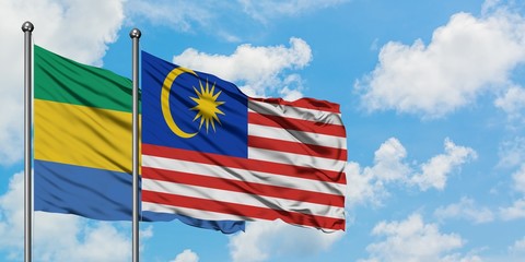 Gabon and Malaysia flag waving in the wind against white cloudy blue sky together. Diplomacy concept, international relations.