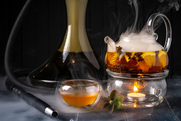 A pot of tea with lemon and Smoking hookah on a dark wooden background. Traditional Arabian shisha with tea.