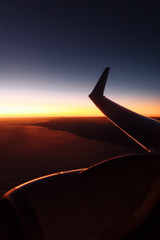 Beautiful view from airplane window on the wing at sunset or sunrise time. Flying above the clouds. Looking through window aircraft during flight in wing with a nice sky. Flight for relax in holiday.