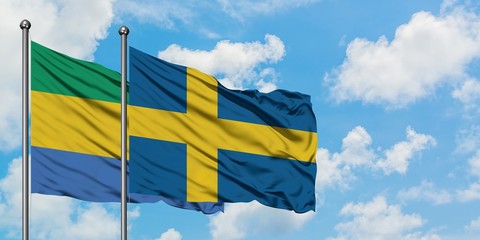 Gabon and Sweden flag waving in the wind against white cloudy blue sky together. Diplomacy concept, international relations.