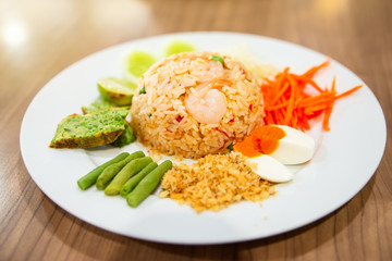 Thai Spicy Shrimp Paste Fried Rice,Mixed vegetable such as carrot,cucumber,Yardlong beans, lime and boiled egg in white dish on wood table