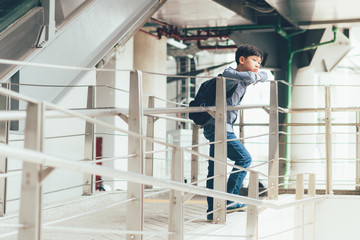 A good looking asian teen student boy in smart casual outfit standing at the beautiful walkway in a train station thinking or waiting for someone. City public transportation, Teenager lifestyle.