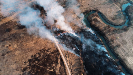 Strong fire in an empty field, heavy smoke from a burning place. The spread of the fire is stopped by a small river.