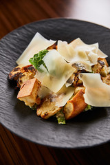 tasty Caesar salad with Parmesan slices served on plate on wooden table