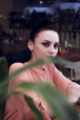 portrait of young woman drinking coffee at table in cafe through the window