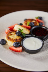 close up view of traditional Ukrainian dish syrniki with strawberry, blueberry served with jam and sour cream