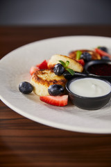 close up view of traditional Ukrainian dish syrniki with strawberry, blueberry served with jam and sour cream