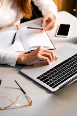 cropped view of woman with credit card, notepad, laptop and smartphone in cafe