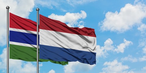 Gambia and Netherlands flag waving in the wind against white cloudy blue sky together. Diplomacy concept, international relations.