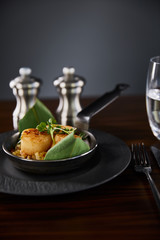 selective focus of delicious grilled scallops with green leaves and microgreens near cutlery, water and pepper, salt shakers