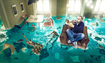 man plays the trumpet in a floating chair in a completely flooded living room. © tiero