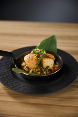delicious grilled scallops with green leaves and microgreens on wooden table on black background