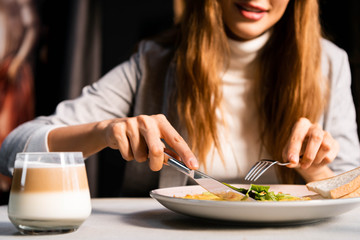 cropped view of woman eating breakfast with glass of coffee in cafe