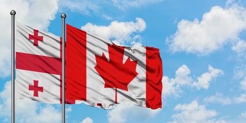 Georgia and Canada flag waving in the wind against white cloudy blue sky together. Diplomacy concept, international relations.