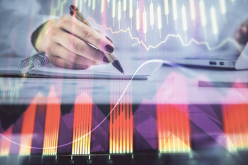 Double exposure of woman's hands making notes with forex graph hologram. Concept technical analysis.