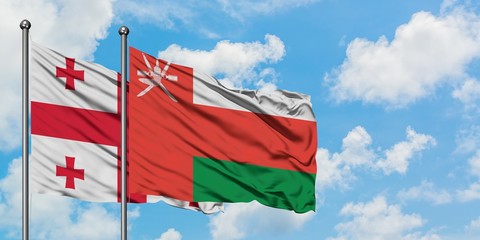 Georgia and Oman flag waving in the wind against white cloudy blue sky together. Diplomacy concept, international relations.