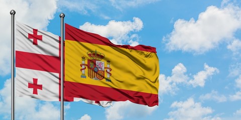 Georgia and Spain flag waving in the wind against white cloudy blue sky together. Diplomacy concept, international relations.