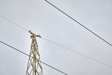 High-voltage powerlines and a detail of the top pf a high-voltage pylon against the gray sky. Seen...