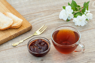 Glass cup of tea, bread, strawberry jam and white jasmine flowers