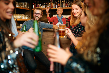 Handsome caucasian waitress staning in bar and wiping glass. Customers drinking beer. Nightlife.