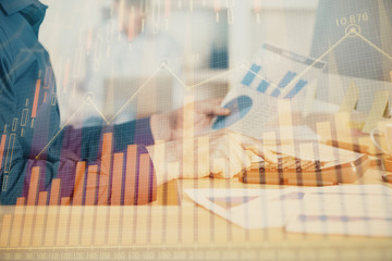 Double exposure of graph with man typing on computer in office on background. Concept of hard work. Closeup.