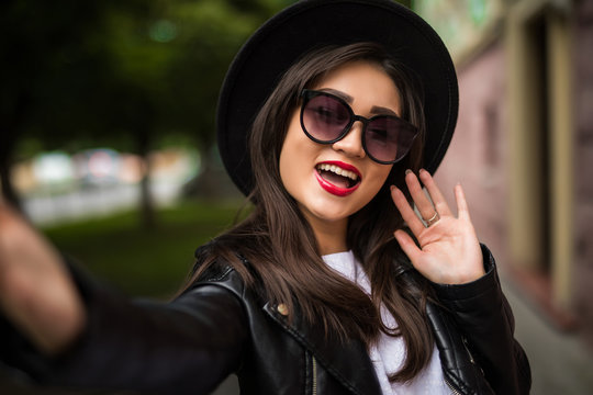 Pretty beautiful smiling Asian woman in hat and sunglasses taking selfie in city street