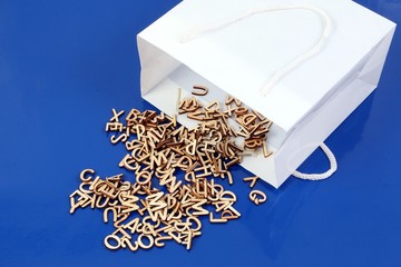 Many small wooden letters fall out of a white bag on a blue background in the studio