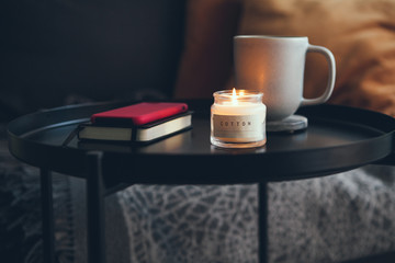 Little black raund table next to the sofa with cup of delicious hot chocalate / cacao drink and candlelight. Relaxing after work mood, offline. Warm natural light, Scandinavian style