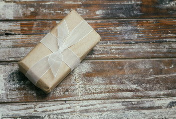 Gift box wrapped in brown craft paper and tie white satin ribbon. Christmas mood. Decorative wood background. Present package. 