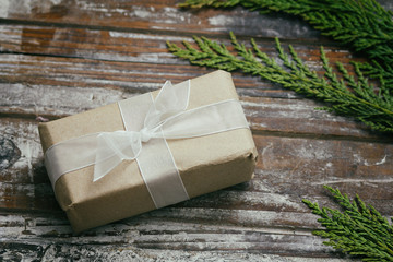Gift box wrapped in brown craft paper and tie white satin ribbon. Christmas mood. Decorative wood background. Present package. 