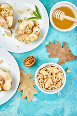 Tasty roast pears with honey and walnuts on white plates on blue background table. Top view.  Flat lay. Copy space.