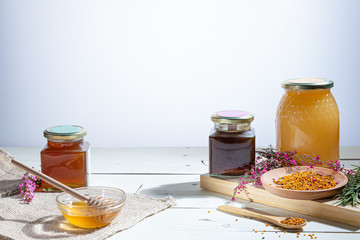 Honey  jars with honey sticks ,flowers and bee pollen on wooden white background