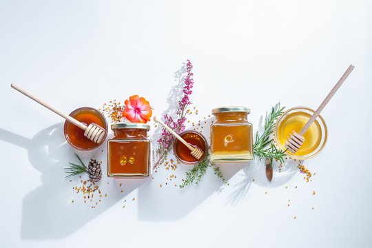 Composition of honey  jars with honey sticks ,flowers and bee pollen on white background