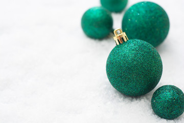 Christmas glitered green baubles, balls isolated on snow. Winter greeting card with copy space.