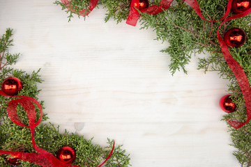 Christmas copy space with pine branches, red organza ribbon and red Christmas baubles on a light wooden background