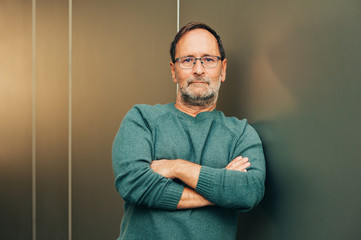 Outdoor portrait of 50 - 55 year old man wearing green pullover and eyeglasses, arms crossed