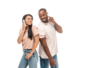Fototapeta premium happy african american couple looking at each other while talking on smartphones isolated on white