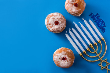 Jewish Hanukkah menorah and sufganiyot donuts on blue background. Top view. Copy space	